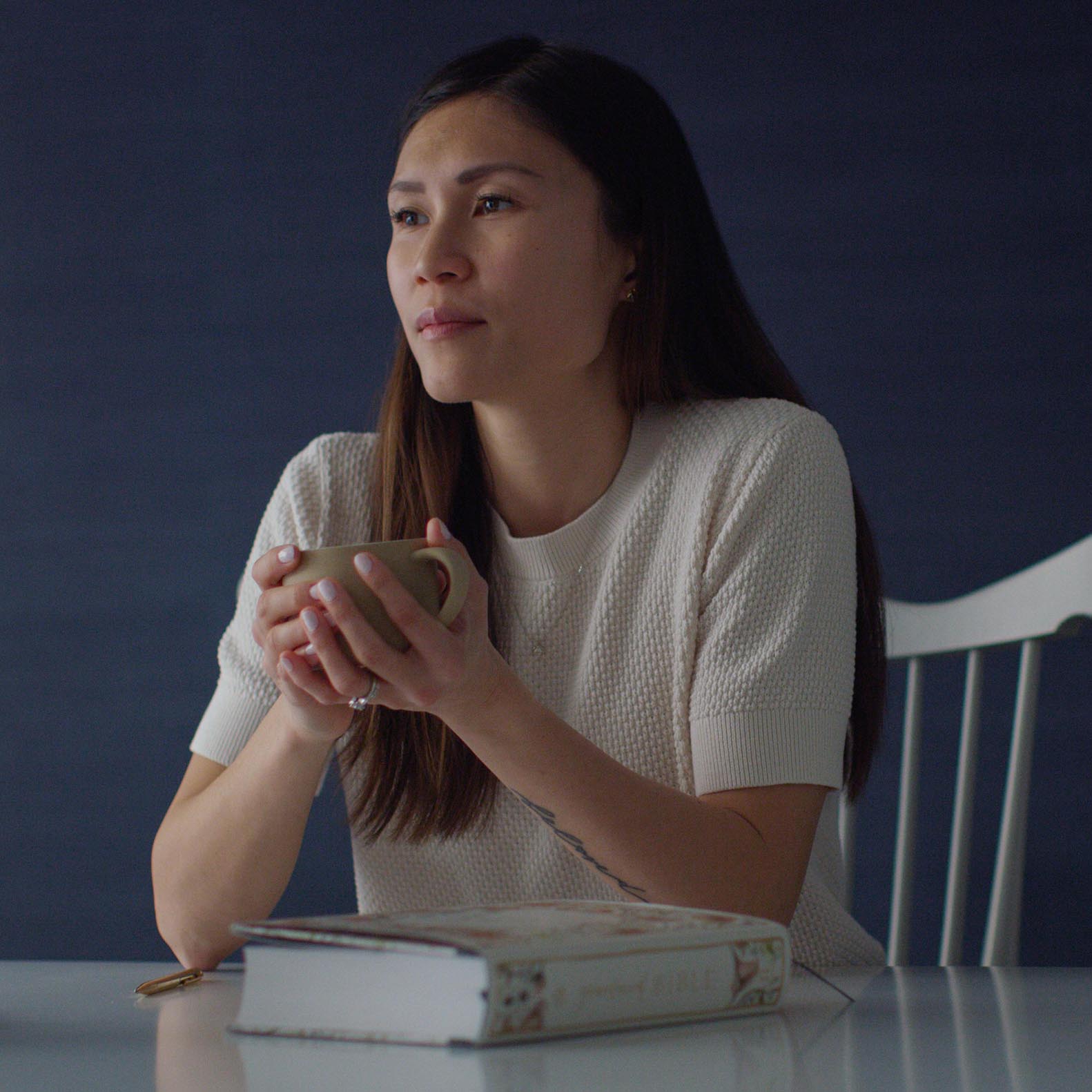 An image of a woman holding a coffee cup while sitting next to a copy of the Gracelaced Bible.