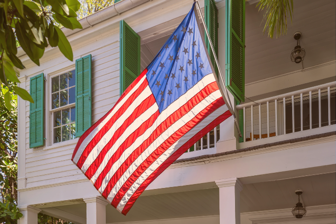 Photo of an older version of the American flag hanging in front of a colonial-style home.
