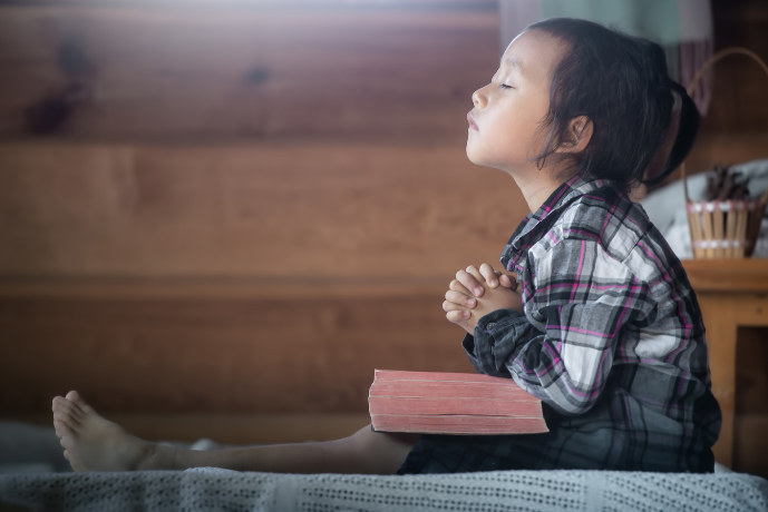 Photo of a little girl sitting with a Bible in her lap and praying.
