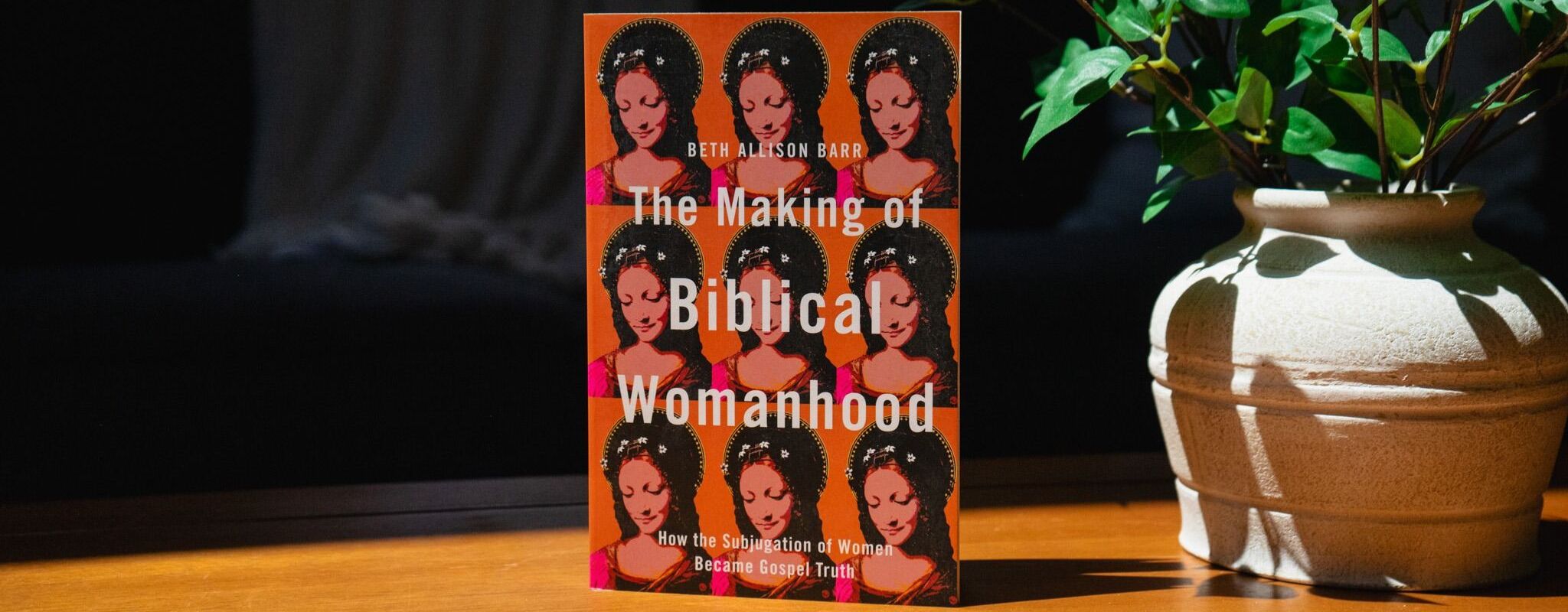 Image of the book "The Making of Biblical Womanhood: How the Subjugation of Women Became Gospel Truth" by Beth Allison Bar, on a wooden table next to a green potted plant.