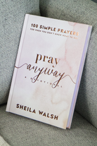 The cover of "Pray Anyway" by Sheila Walsh on the cushion of a gray couch.