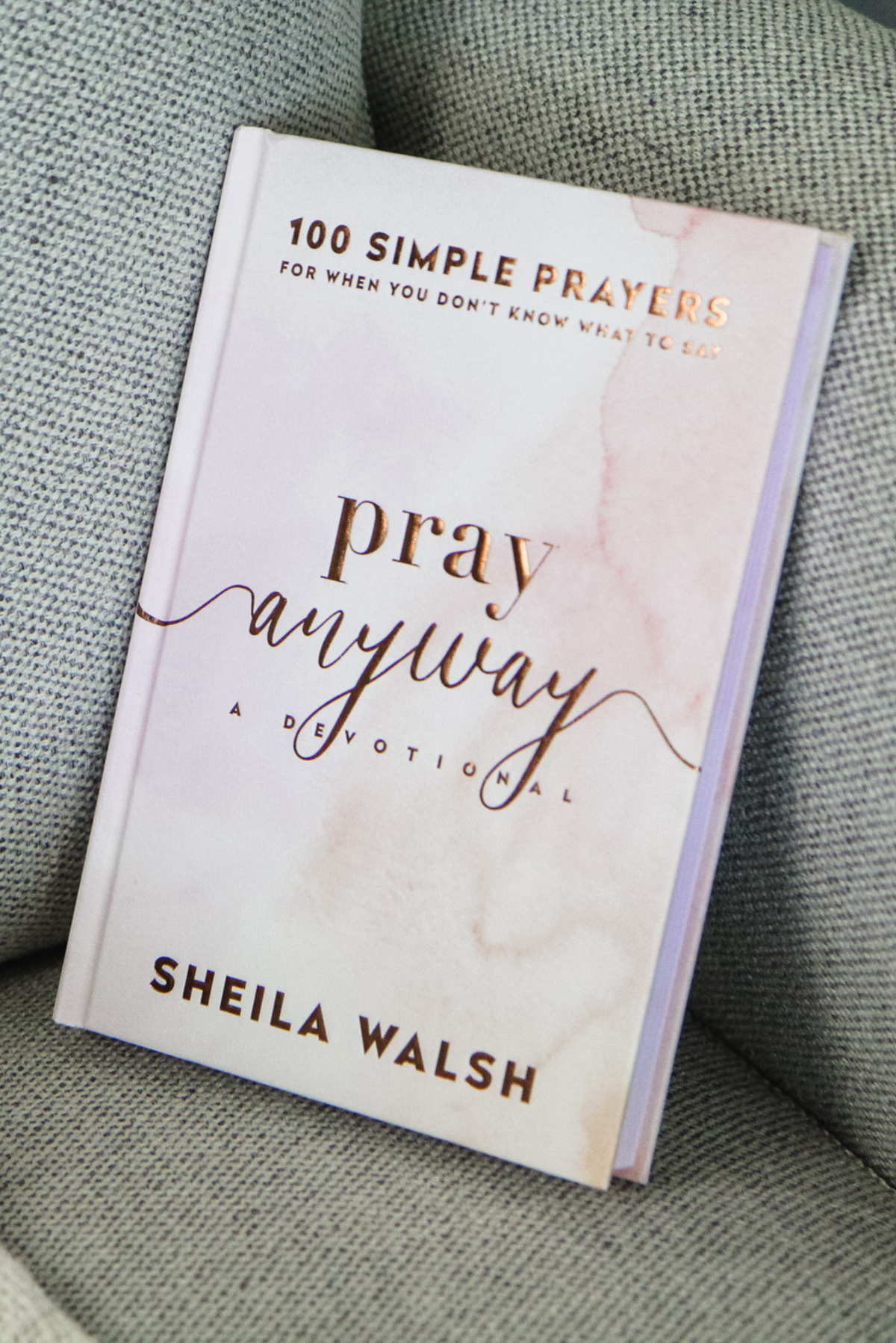 The cover of "Pray Anyway" by Sheila Walsh on the cushion of a gray couch.